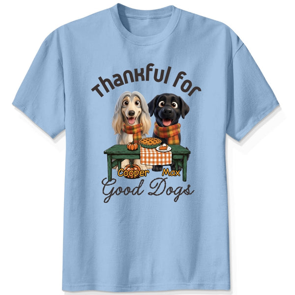 A blue short-sleeve crewneck t-shirt featuring a graphic print of custom dogs sitting at a table with autumn food, with the text 'Thankful for Good Dogs' and custom dog's names written around the illustration.