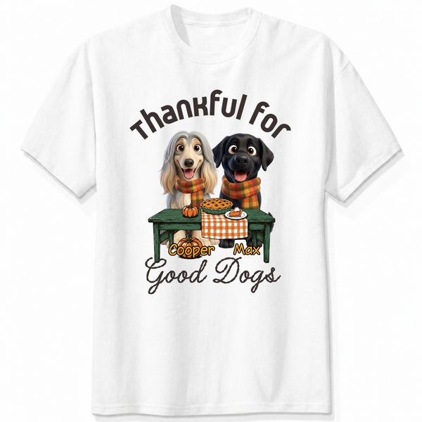 A white short-sleeve crewneck t-shirt featuring a graphic print of custom dogs sitting at a table with autumn food, with the text 'Thankful for Good Dogs' and custom dog's names written around the illustration.