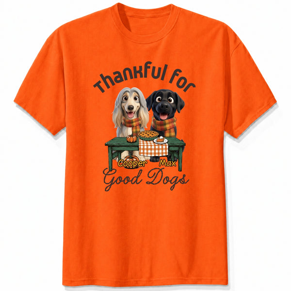 An orange short-sleeve crewneck t-shirt featuring a graphic print of custom dogs sitting at a table with autumn food, with the text 'Thankful for Good Dogs' and custom dog's names written around the illustration.