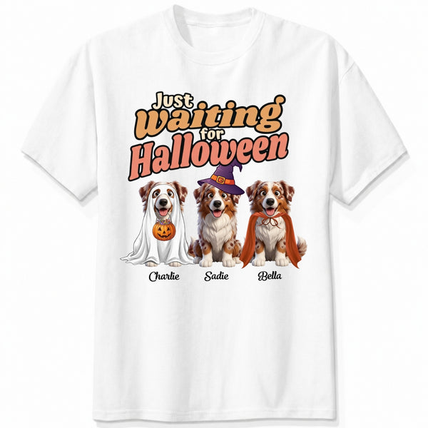 A white short-sleeve crewneck t-shirt featuring dogs dressed in costumes and the text 'Just Waiting for Halloween'.